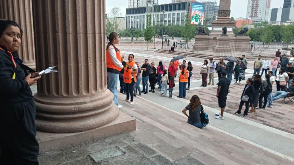 Group of People Gathered at a Monument Steps, Some Wearing Orange Safety Vests, Listening to a Speaker on a Pedestal. - Justicia Regia