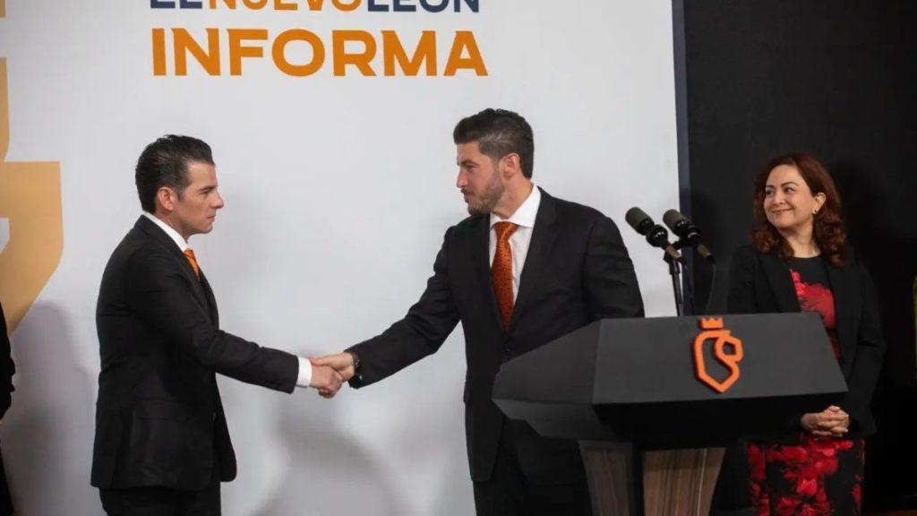 Two Businessmen in Suits Shake Hands on a Stage Beside a Black Podium with an Orange Logo, As a Woman Smiles Nearby Under an ‘informa’ Banner. - Justicia Regia