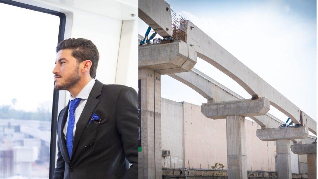Businessman in a Black Suit and Blue Tie Stands by a Window, with a Construction Site Featuring Concrete Beams in the Background. - Justicia Regia