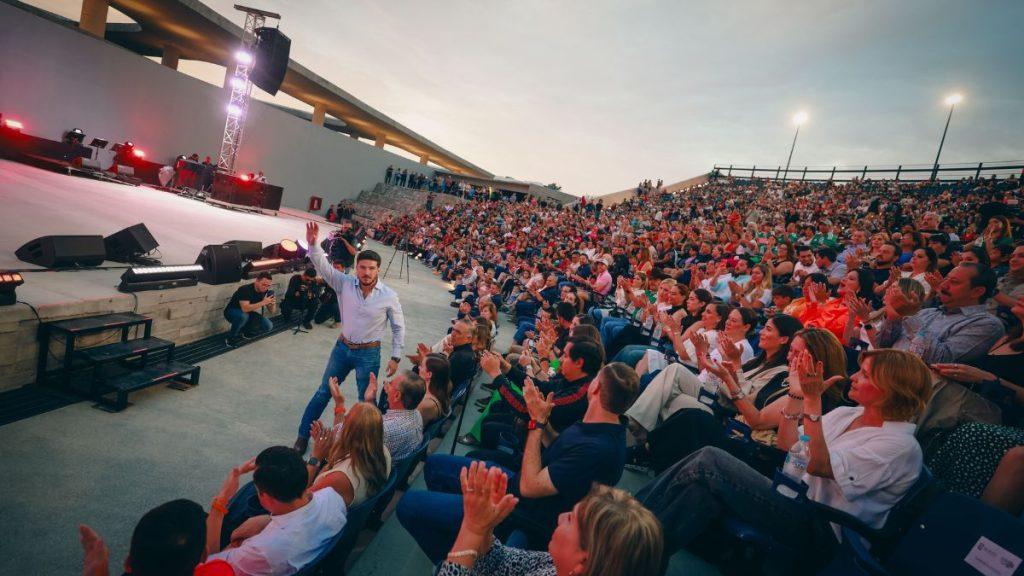 Parque-del-agua-en-guadalupe - Justicia Regia Man in a Light Shirt Waves to a Cheering Crowd from an Outdoor Stage at Dusk in Front of a Large Audience. - Justicia Regia