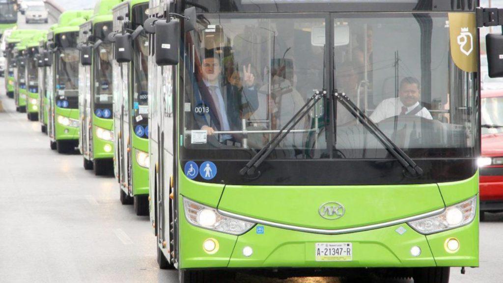 Bloque 2- Julio 68 - Justicia Regia Front Green Bus with a Driver Waving from the Window; a Line of Matching Buses Follows on a City Street Professional Fleet Style. - Justicia Regia