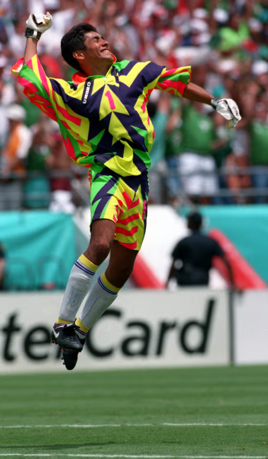 Image - Justicia Regia Soccer Goalkeeper in a Bright Neon Jersey Jumping in Celebration on the Field, Arms Raised As Fans Cheer in the Background. - Justicia Regia