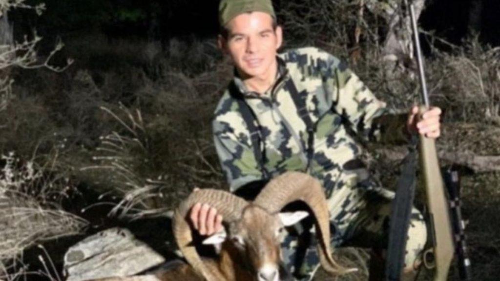 Hunter in Camouflage Posing with a Ram, Holding Its Horns While a Rifle Rests Nearby in a Rocky, Brushy Outdoor Setting. - Justicia Regia
