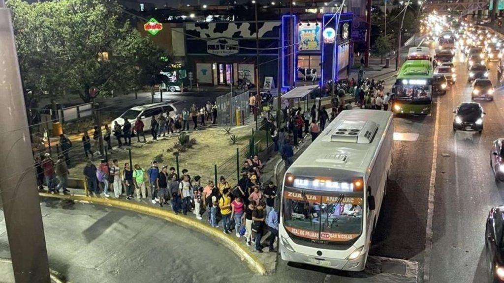 Samuel-presume-que-sobran-camiones 1 - Justicia Regia Nighttime Street Scene with a Long Queue of People Waiting to Board a White Bus by the Curb. - Justicia Regia